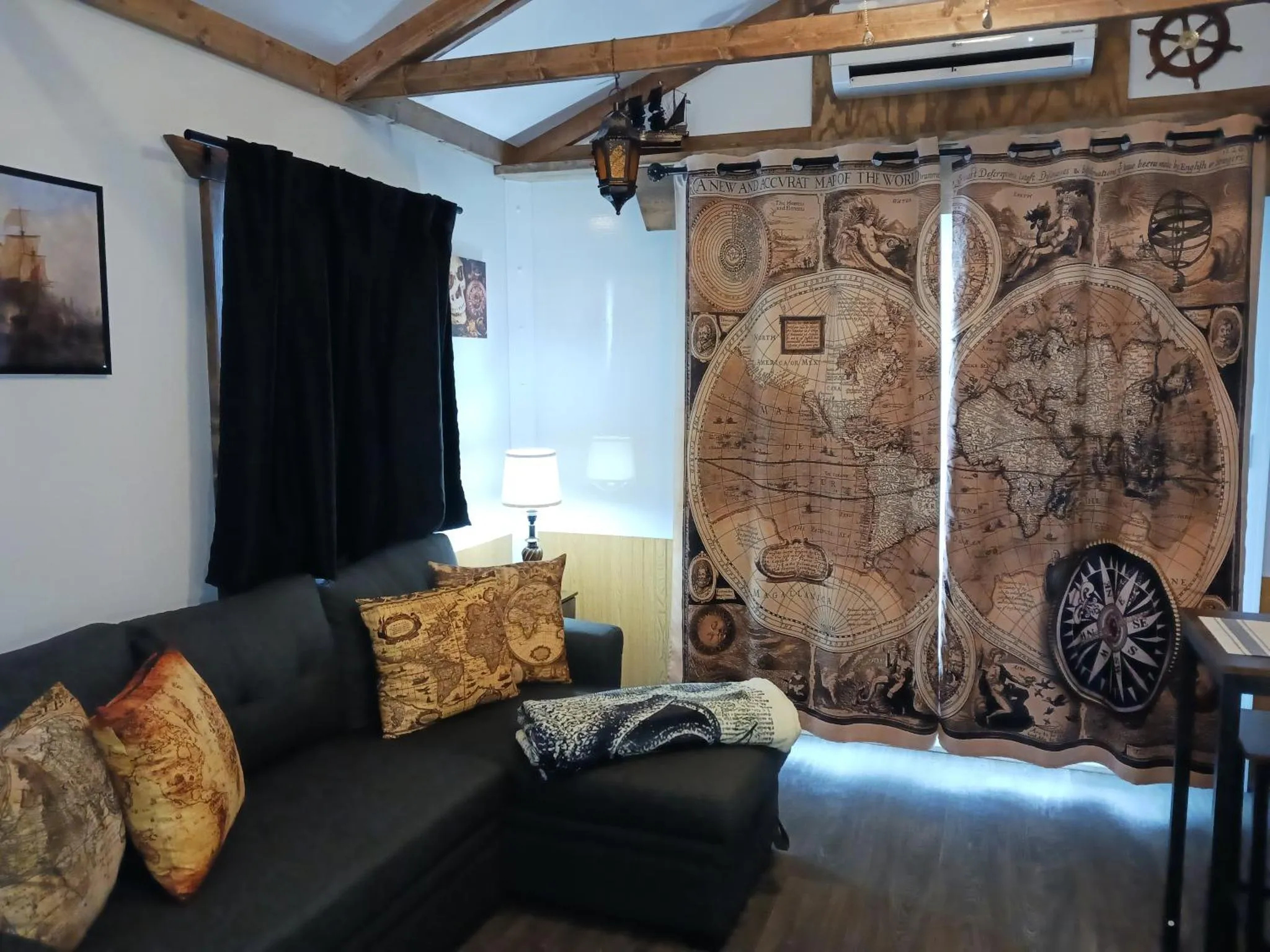 Un canapé noir avec des coussins se trouve dans une pièce décorée d'une carte marine et de rideaux sombres.