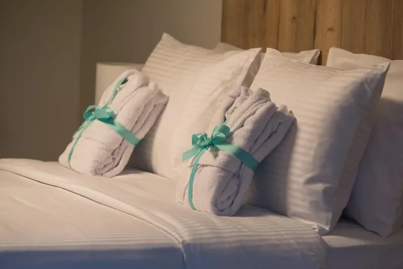 Un lit recouvert de draps blancs avec des oreillers et des peignoirs pliés.