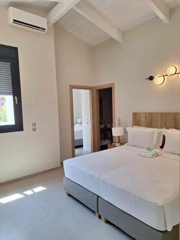 Une chambre lumineuse avec un grand lit et une porte ouverte sur une autre pièce.