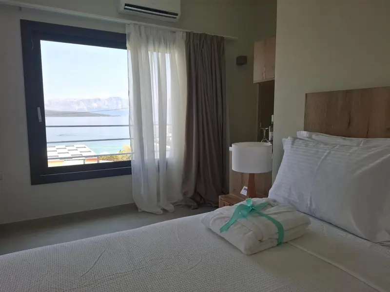 Une chambre lumineuse avec un lit fait et une vue sur la mer par une grande fenêtre.