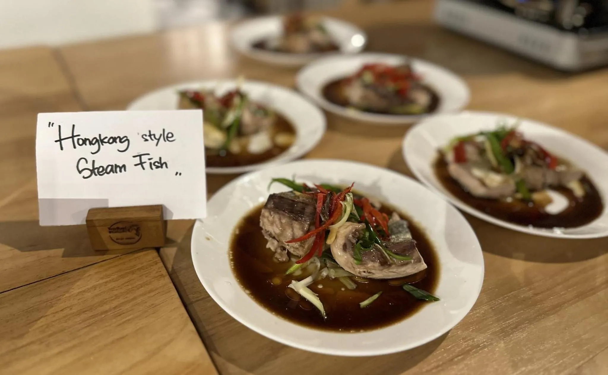 Assiettes de poisson cuit à la vapeur, accompagnées d'une sauce sombre et de légumes.