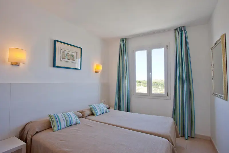 Chambre lumineuse avec deux lits simples et vue sur l'extérieur.