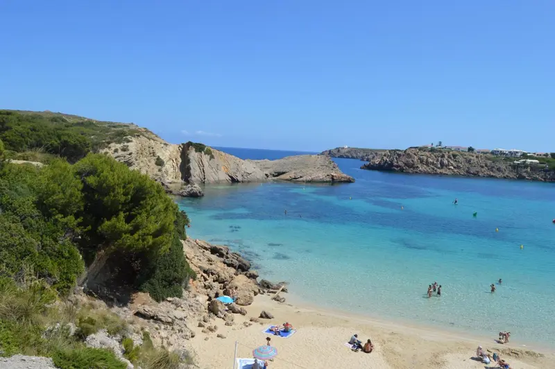 Une plage de sable fin bordée d'une eau turquoise et de rochers.