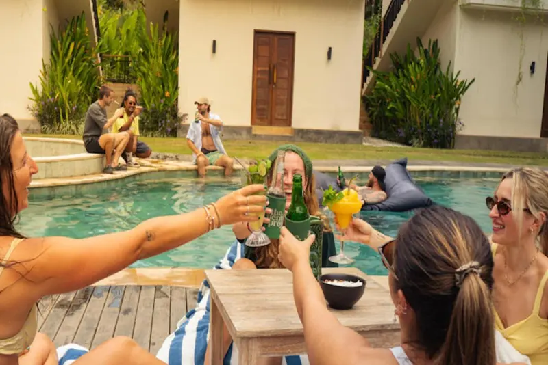 Des personnes se retrouvent autour d'une piscine ensoleillée, échangeant des verres.