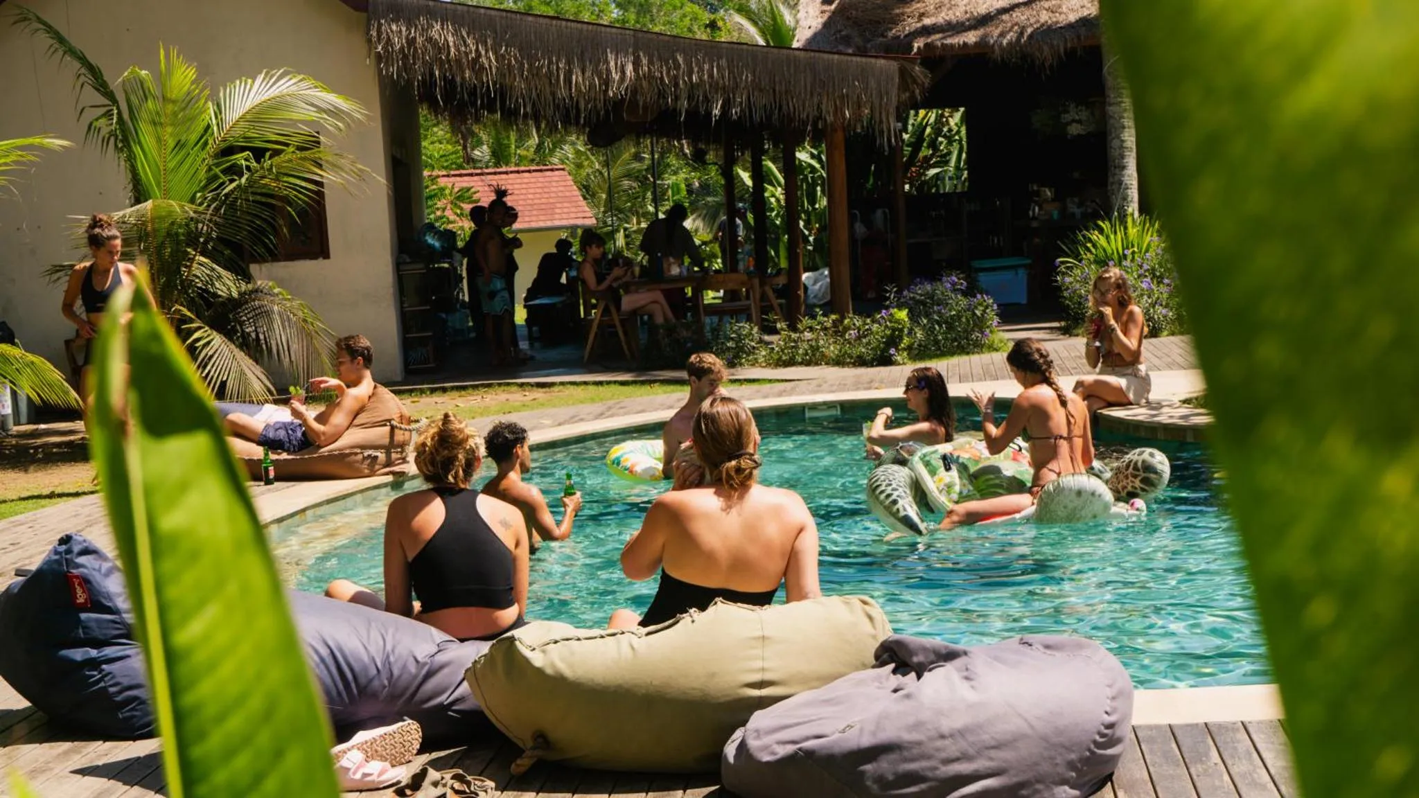 Des personnes se détendent au bord d'une piscine ensoleillée, entourée de végétation tropicale.