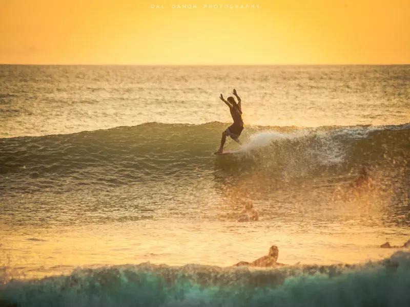 Un surfeur s'élance sur une vague au coucher du soleil.