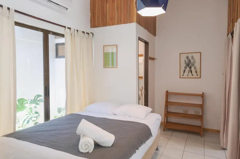 Une chambre lumineuse avec un lit fait et des rideaux clairs.