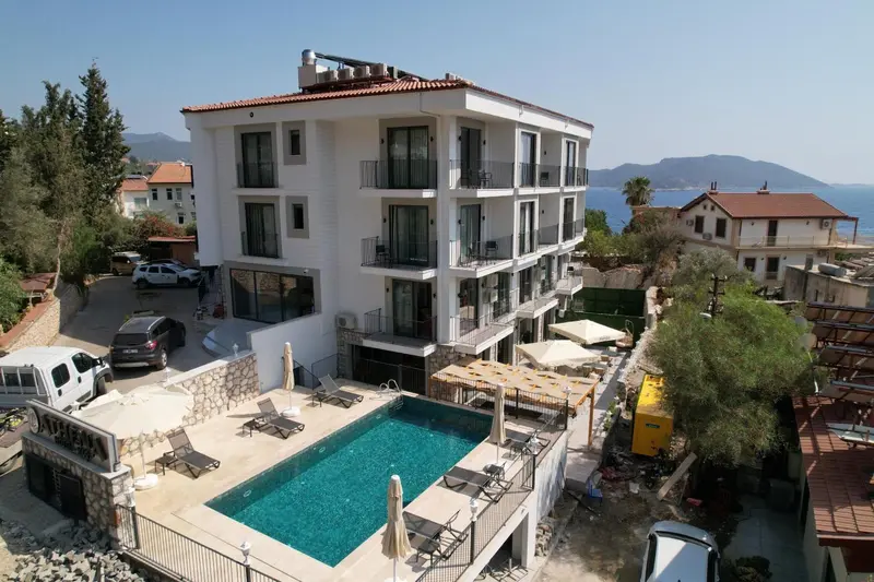 Bâtiment blanc à plusieurs étages avec piscine et transats en contrebas.