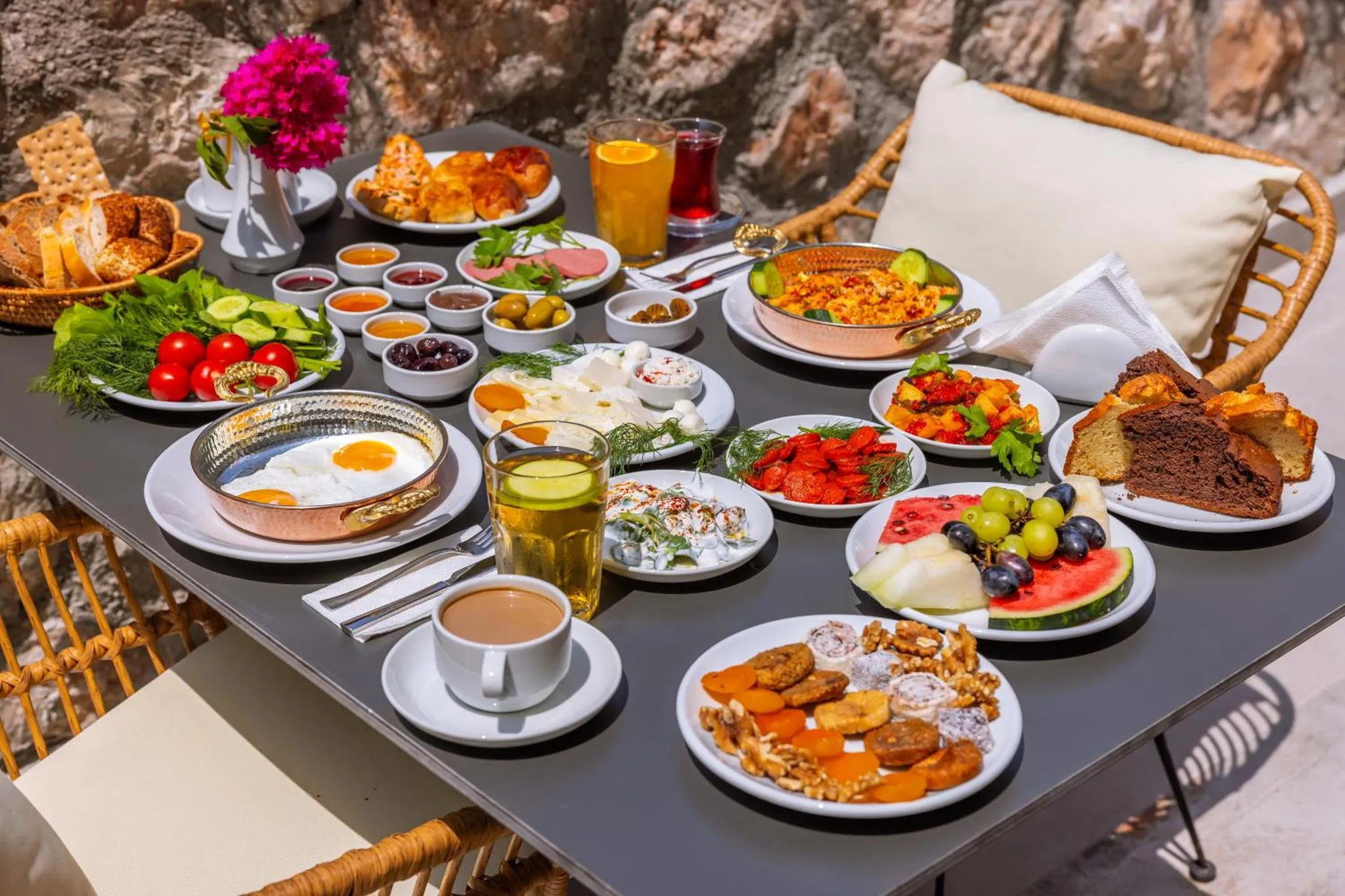 Table garnie de divers plats et boissons sur une terrasse ensoleillée.
