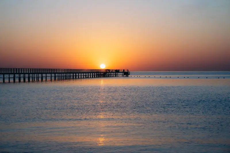 Un ponton s'avance sur une mer calme au coucher du soleil.