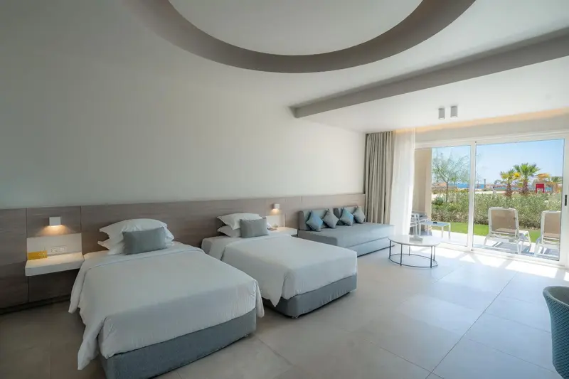 Chambre lumineuse avec lits jumeaux et canapé face à une baie vitrée.