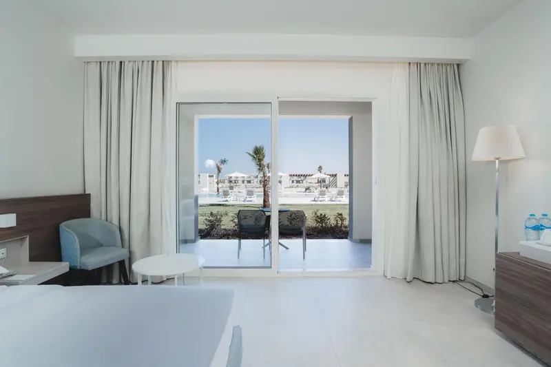 Chambre lumineuse avec vue sur une terrasse et une piscine.