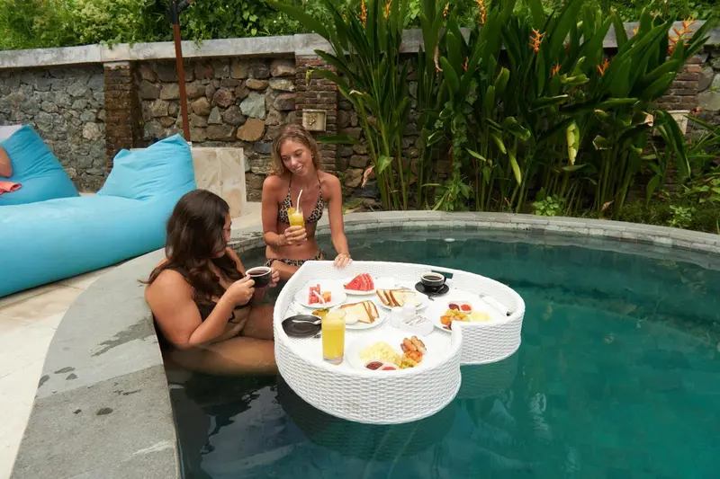 Deux femmes dégustent un petit-déjeuner sur un plateau dans une piscine.