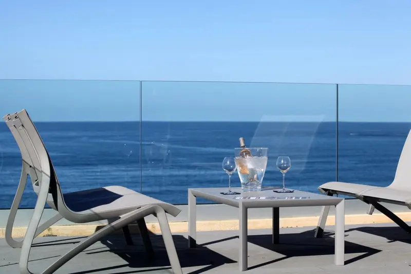 Deux chaises longues et une table basse avec une bouteille et des verres sur une terrasse ensoleillée.