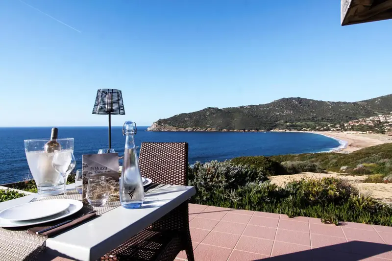 Une table est dressée sur une terrasse avec vue sur la mer et les collines.