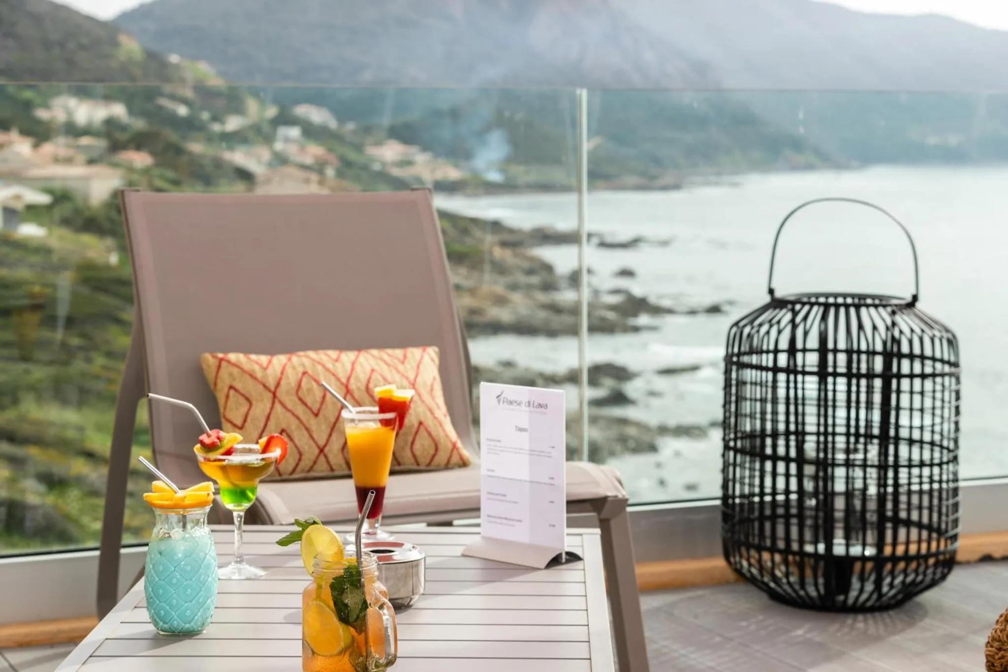 Une table basse avec des boissons colorées sur une terrasse ensoleillée avec vue sur la mer.