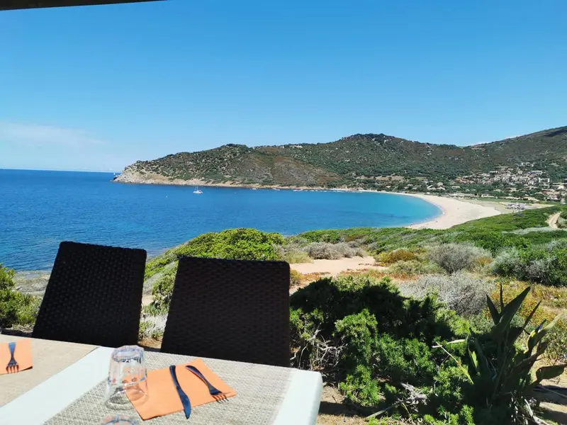 Vue sur une plage et des collines depuis une terrasse de restaurant.