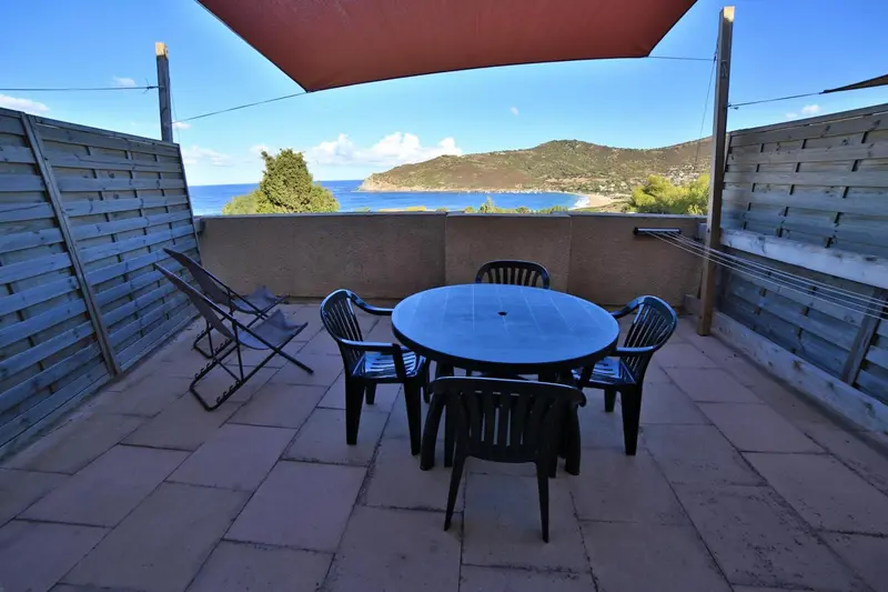 Terrasse carrelée avec table et chaises, vue sur la mer et les collines.