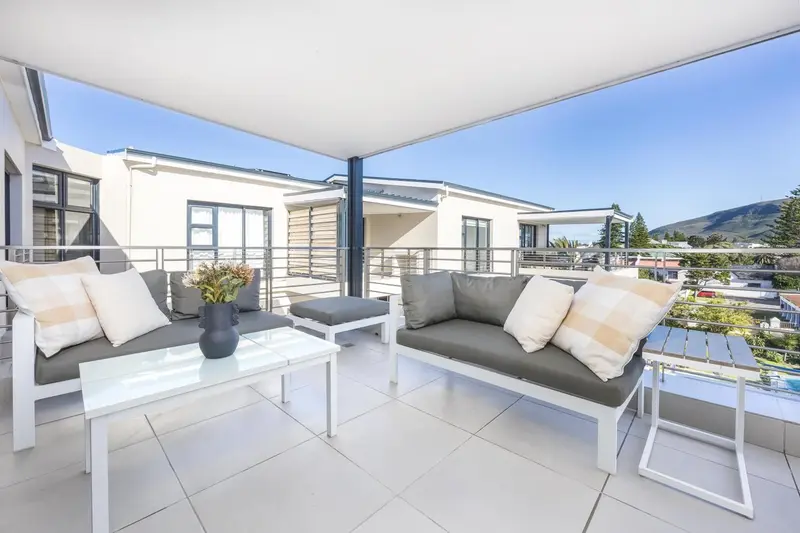 Salon d'extérieur avec canapés et table basse sur une terrasse ensoleillée.