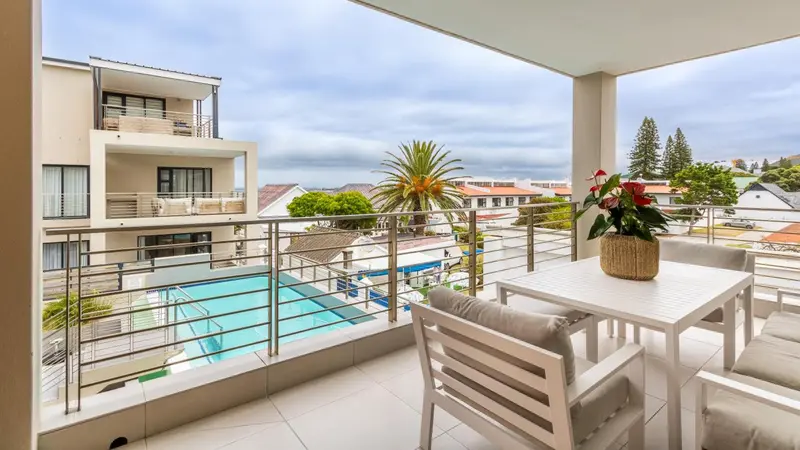 Terrasse aménagée avec mobilier blanc donnant sur une piscine et un paysage urbain.