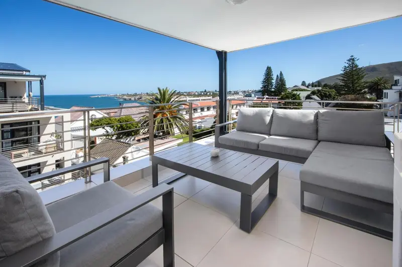 Terrasse aménagée avec canapés et table basse donnant sur une vue urbaine et la mer.