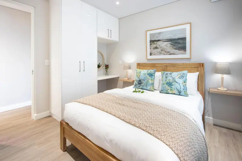 Une chambre lumineuse avec un grand lit et des meubles blancs.