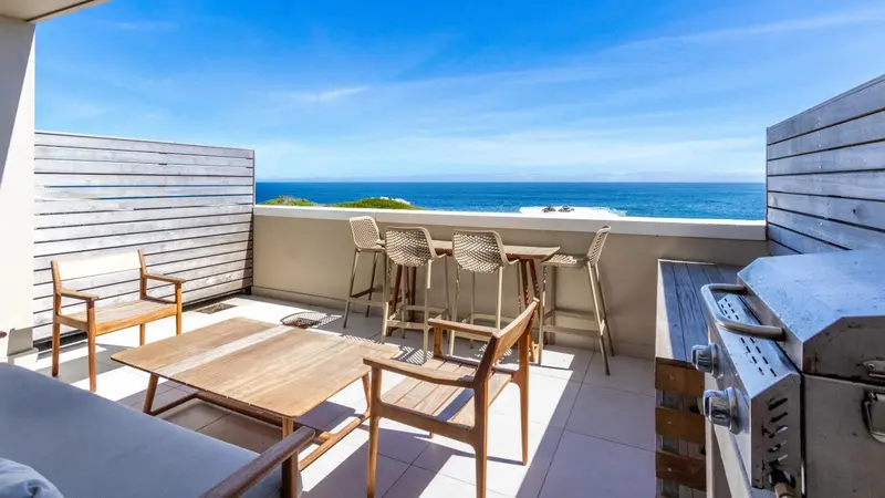 Terrasse aménagée avec mobilier de jardin et barbecue face à la mer.