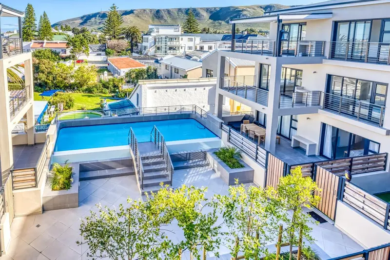 Vue aérienne d'une piscine rectangulaire entourée d'une terrasse et de bâtiments modernes.