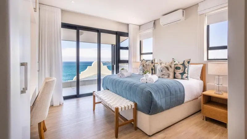 Une chambre lumineuse avec un grand lit et un accès à un balcon avec vue sur la mer.