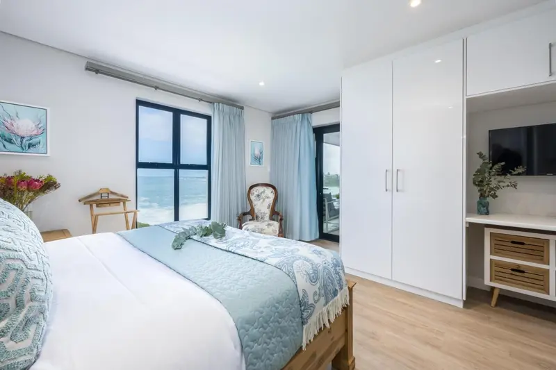 Une chambre lumineuse avec un lit recouvert d'une couverture décorative et un fauteuil près d'une fenêtre.