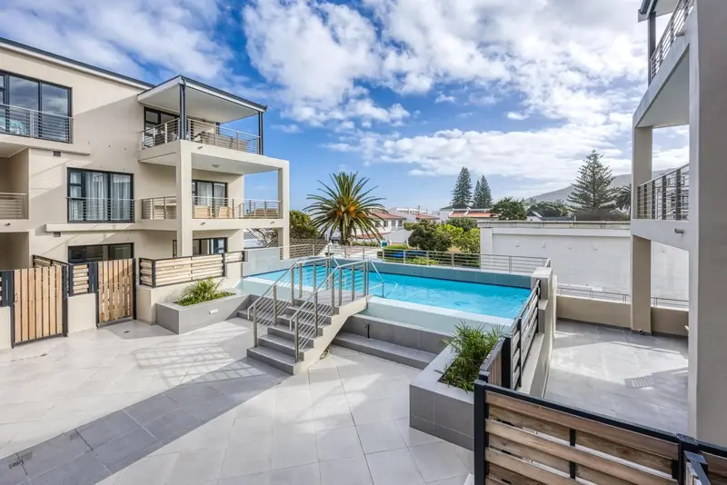 Une piscine rectangulaire est entourée d'une terrasse carrelée et de bâtiments modernes.