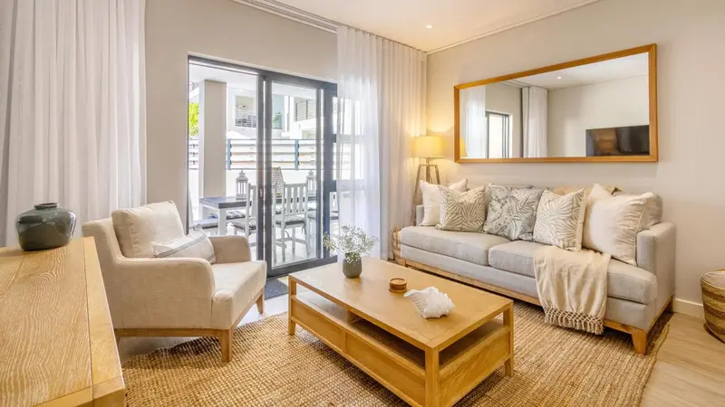 Un salon clair avec un canapé et des fauteuils, donnant sur une terrasse.