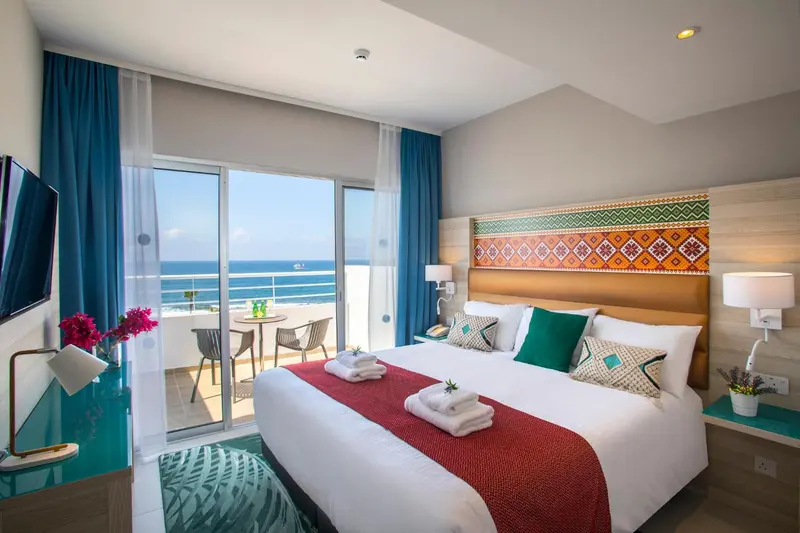 Chambre lumineuse avec un grand lit et une vue sur la mer depuis un balcon.