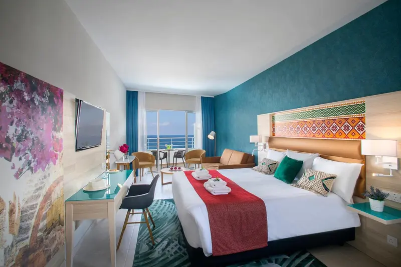 Chambre lumineuse avec un grand lit et un canapé face à la mer.