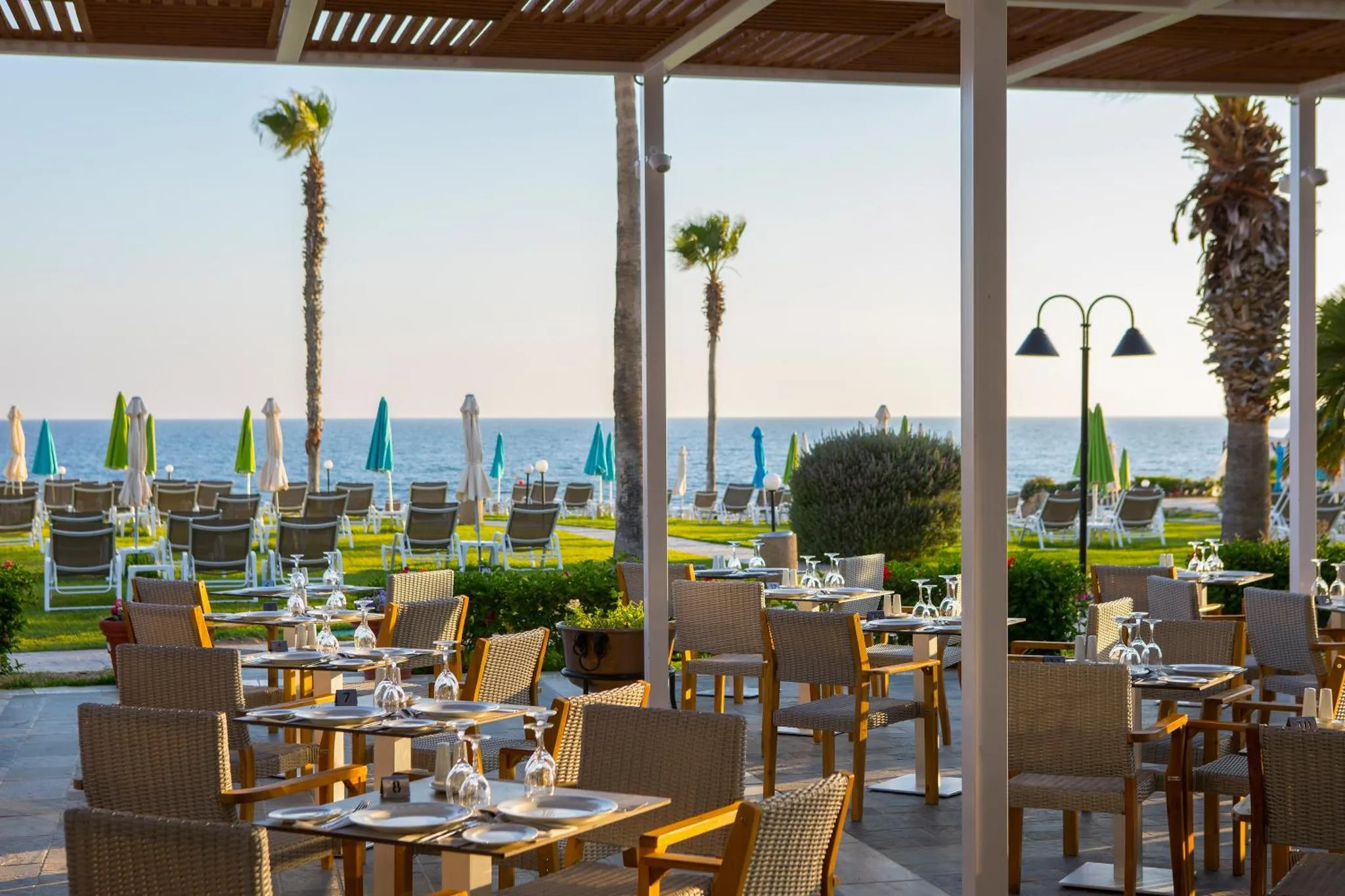 Terrasse ombragée avec tables dressées face à la mer et à la plage.