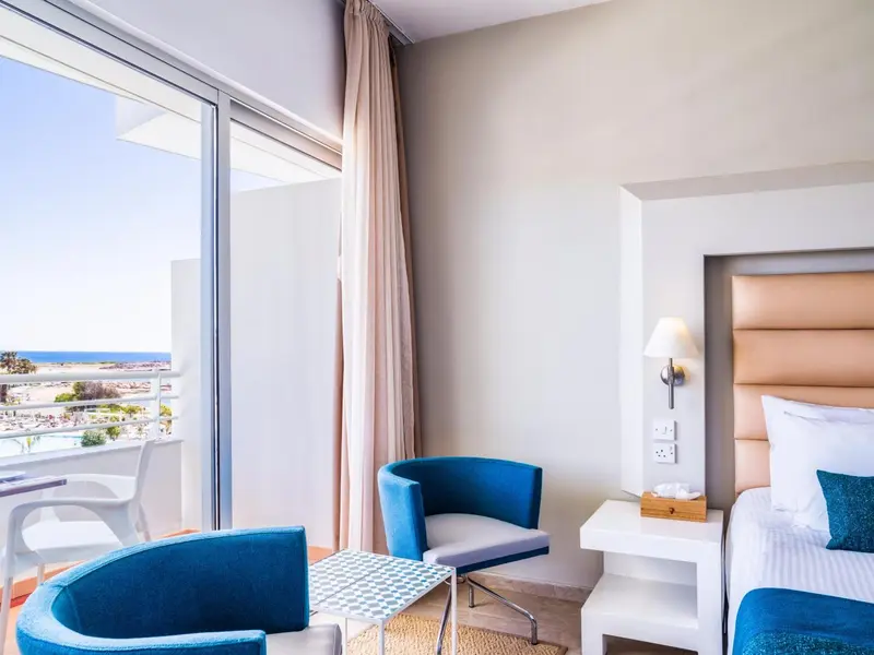 Une chambre lumineuse avec un coin salon et une vue sur la mer.