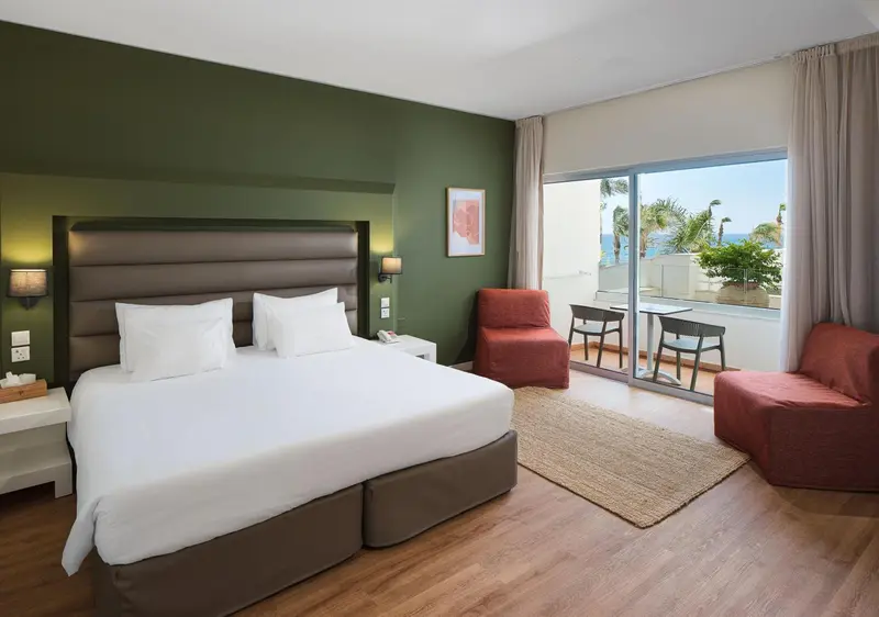 Une chambre lumineuse avec un grand lit et un coin salon donnant sur une terrasse.