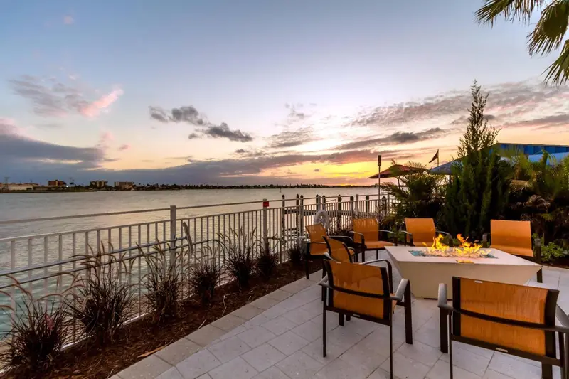 Terrasse avec mobilier d'extérieur face à un plan d'eau au coucher du soleil.