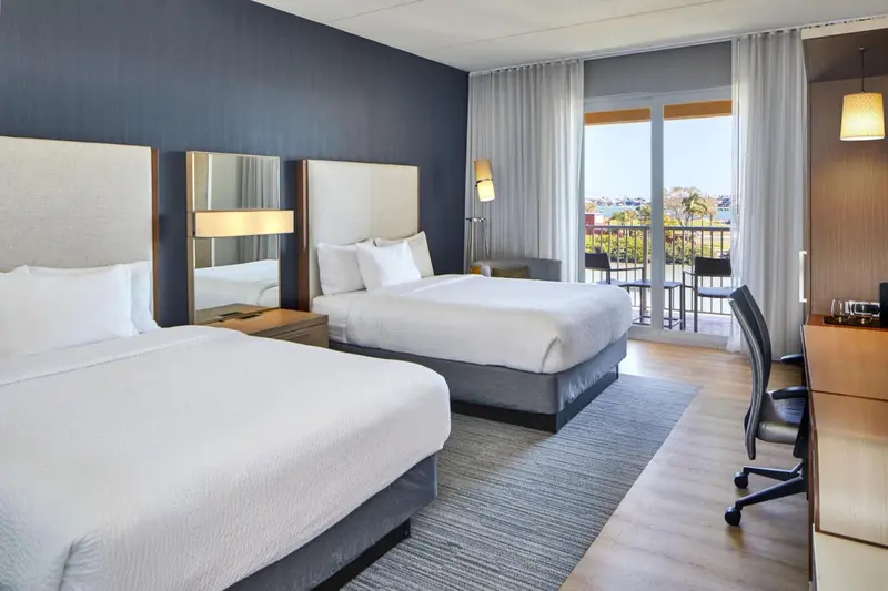 Une chambre d'hôtel lumineuse avec deux lits et un accès à un balcon.