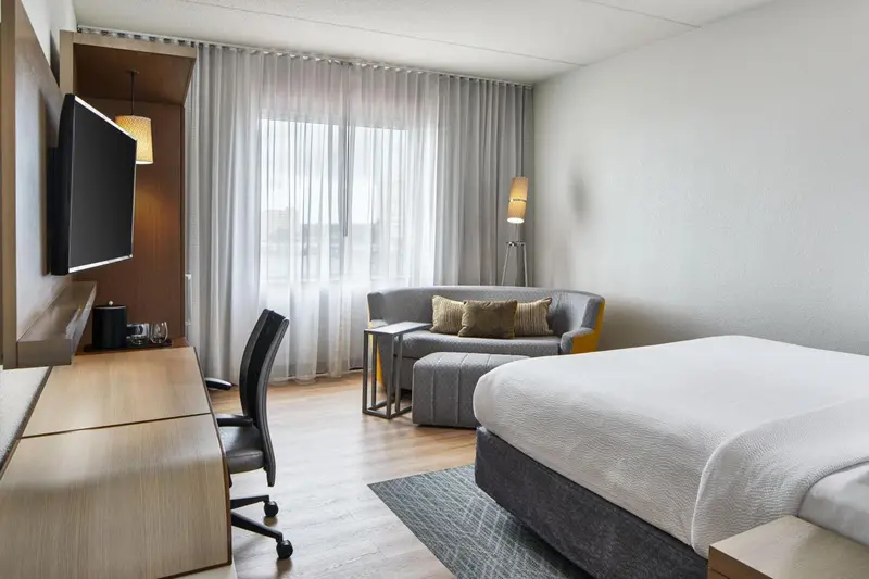 Une chambre lumineuse avec un lit, un bureau et un coin salon près d'une fenêtre.
