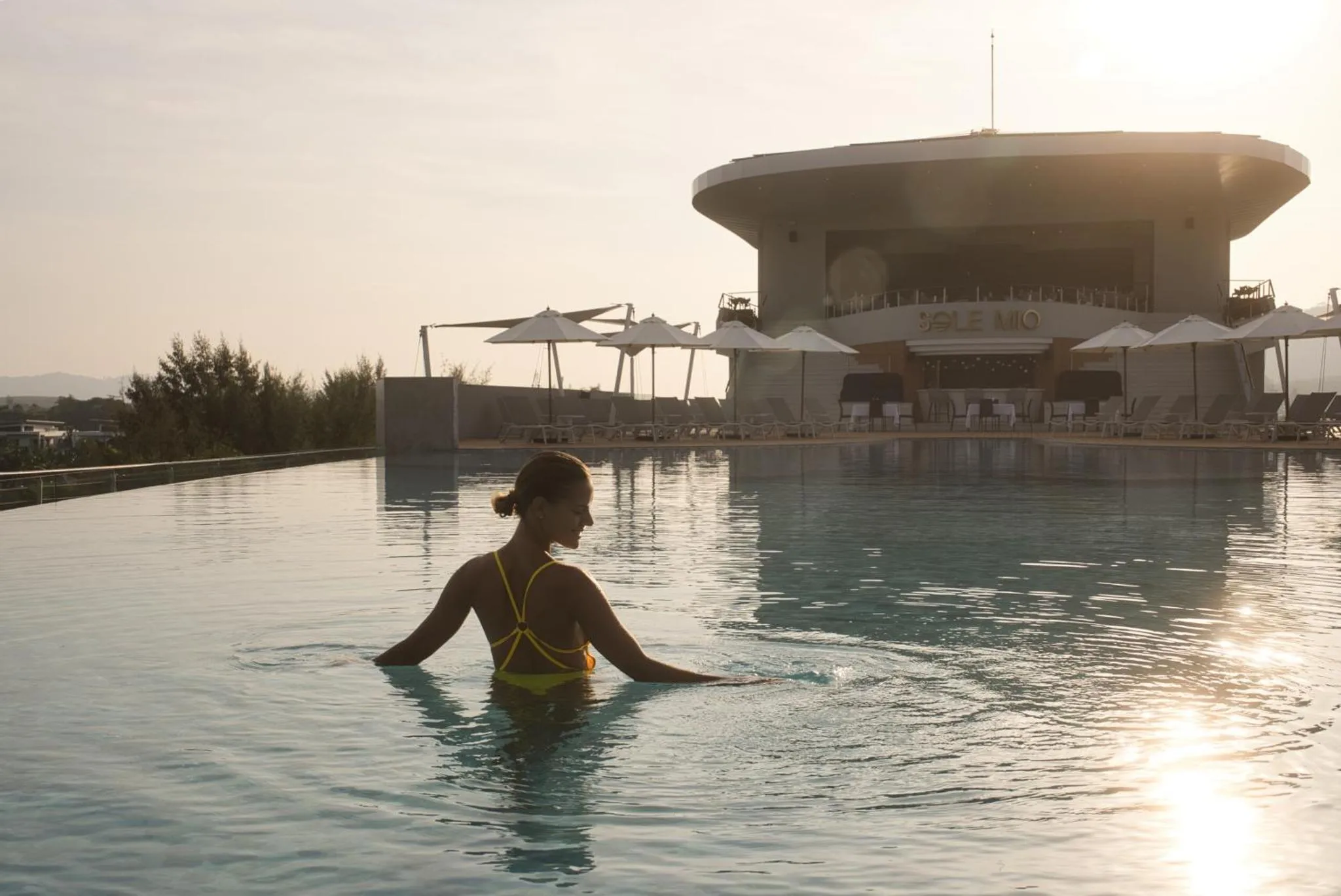 Une femme sort d'une piscine à débordement au coucher du soleil.