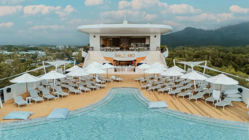 Terrasse avec transats et piscine au premier plan, vue sur la végétation et les montagnes.
