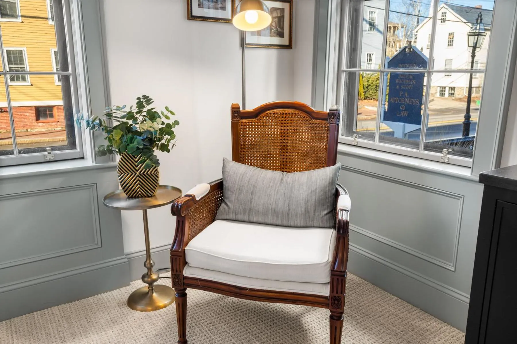 Un fauteuil en bois et un coussin gris reposent près d'une fenêtre.