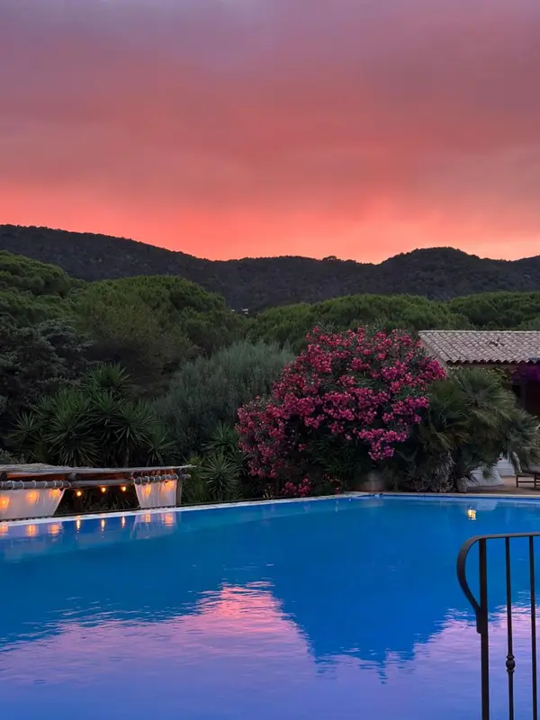 Une piscine reflète les couleurs d'un coucher de soleil sur un paysage vallonné.