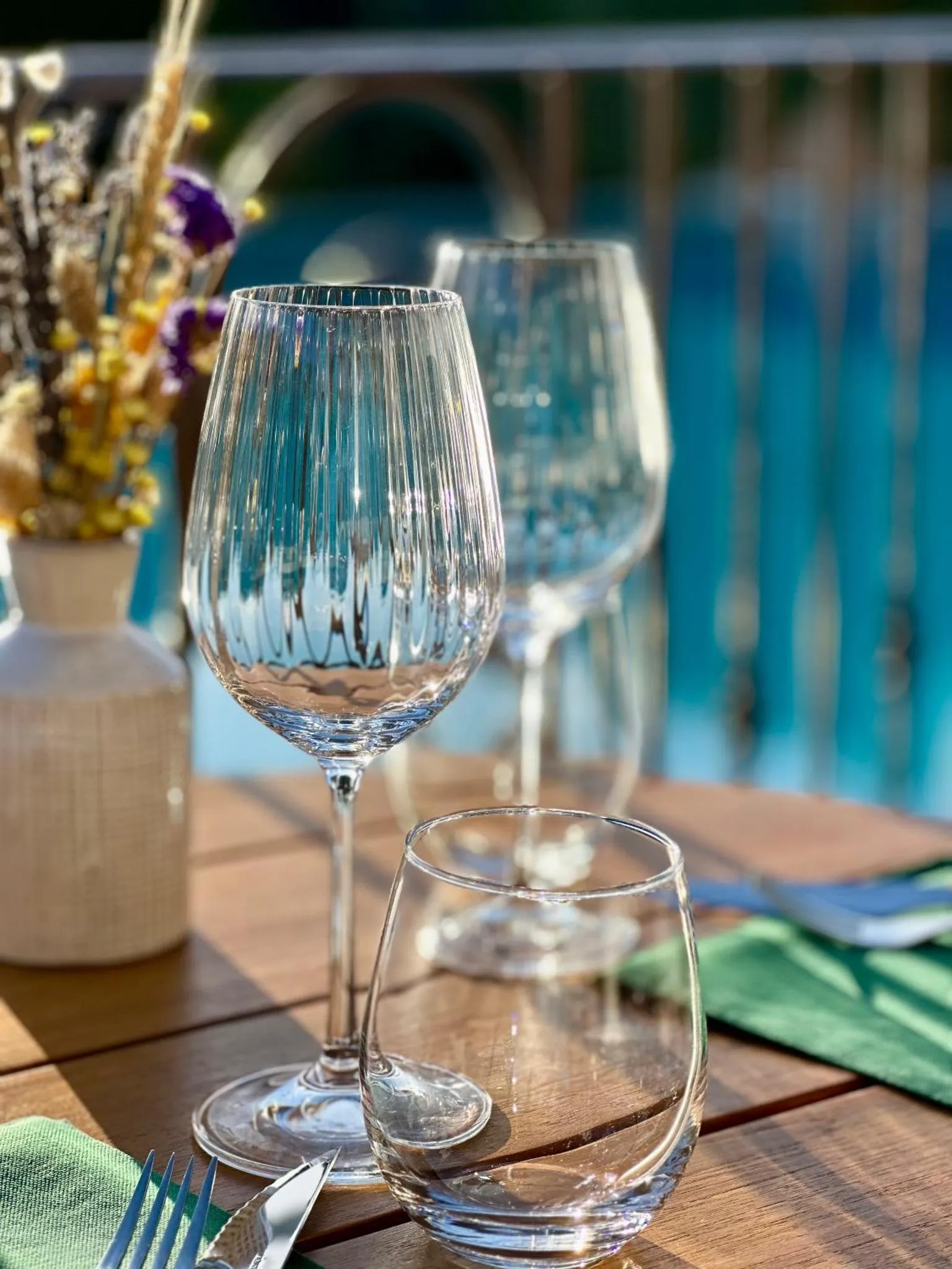 Verres à vin et couverts sur une table en bois près d'une piscine.