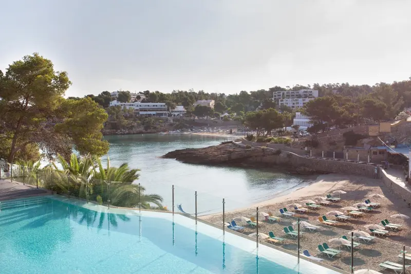 Vue d'une piscine turquoise surplombant une crique de sable et une plage ensoleillée.