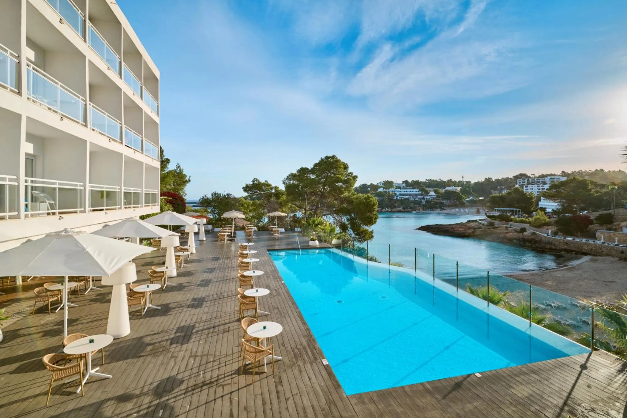 Terrasse avec tables et chaises près d'une piscine et vue sur la mer.