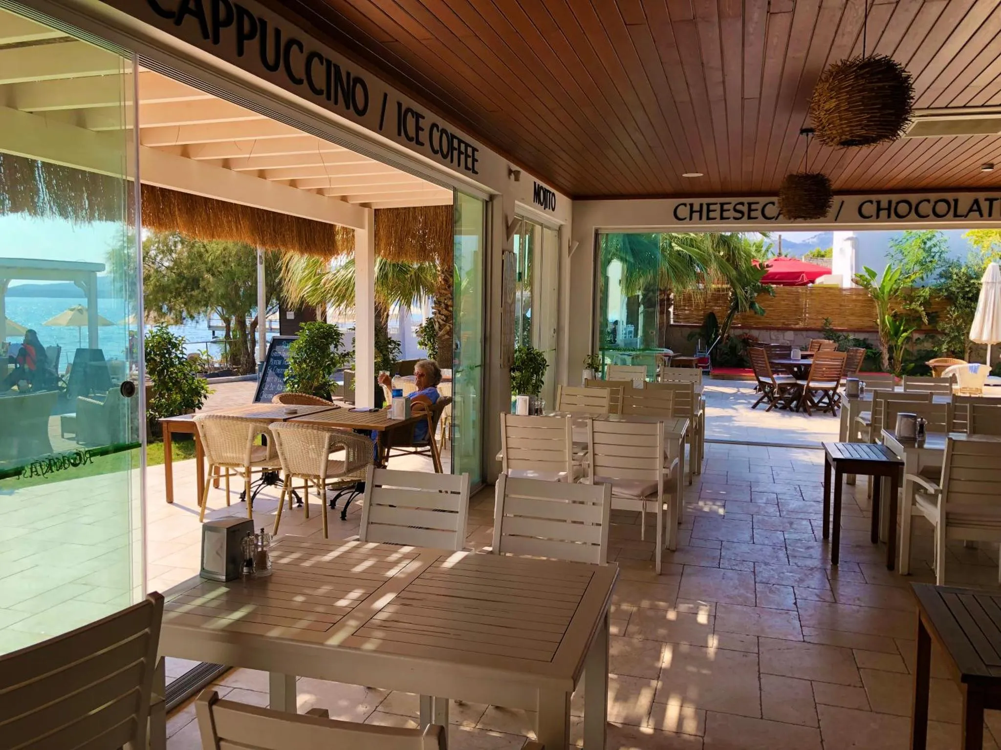 Terrasse ombragée avec tables et chaises près d'un bar en bord de mer.