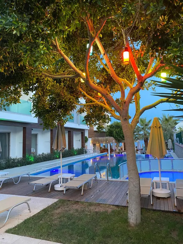 Une piscine bordée de transats et d'une terrasse illuminée par des guirlandes.
