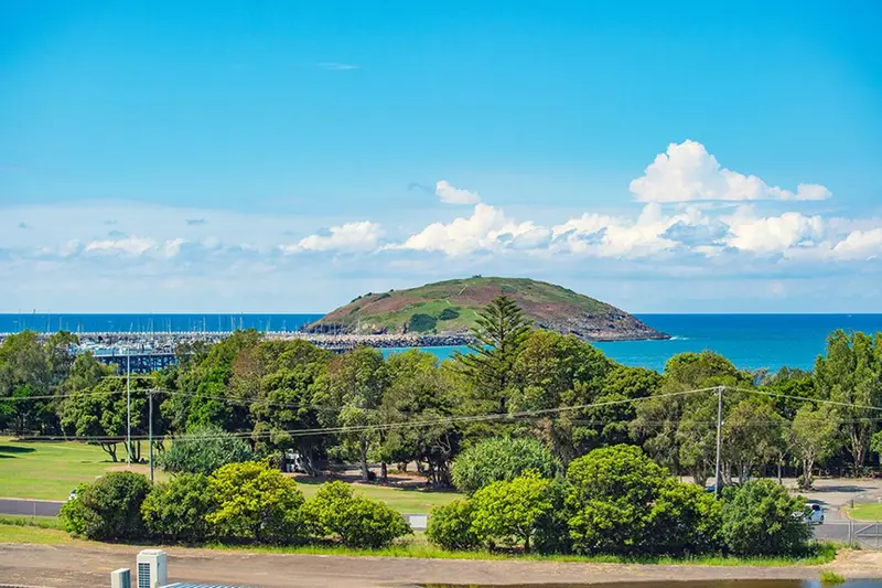 Vue d'une île verdoyante au large d'une côte arborée sous un ciel nuageux.